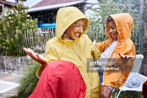 happy mother with son in rainy garden wearing raincoats - lluvia fotografías e imágenes de stock