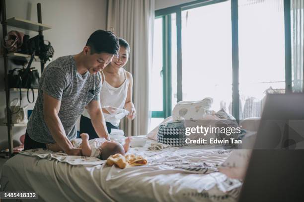 asian chinese parents changing diapers for their baby boy on bed in the morning - adult diaper stockfoto's en -beelden