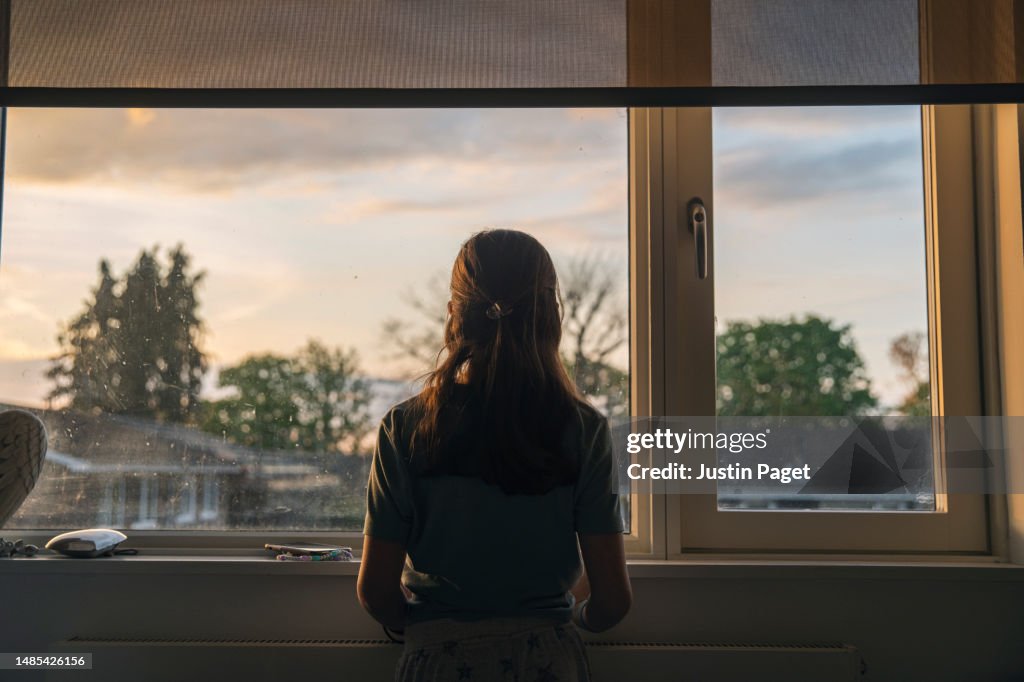 Powerful portrait of a young girl looking out of her window at dusk