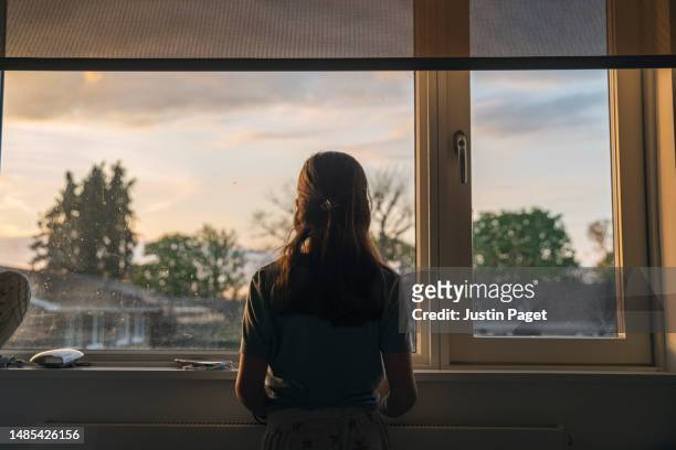 powerful portrait of a young girl looking out of her window at dusk - white bedroom stock pictures, royalty-free photos & images