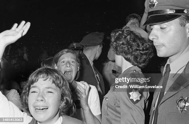 Fans and police officers at a Beatles concert at the Cow Palace in Daly City, near San Francisco, California, during their Summer 1964 United States...