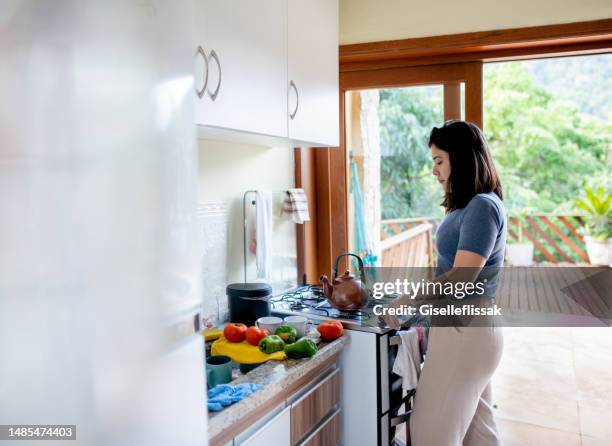 young woman cooking in kitchen at home - kettle kitchen stock pictures, royalty-free photos & images