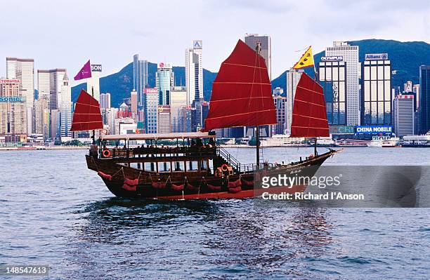tourist boat (junk) on victoria harbour with hong kong island skyline (wan chai) in background. - wooden boat stock pictures, royalty-free photos & images
