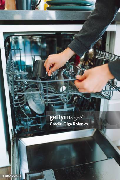 streamlined kitchen tasks with dishwasher. cropped housewife hands putting plates and mugs in basket of dishwasher machine in the kitchen. front view - dishwasher front stockfoto's en -beelden