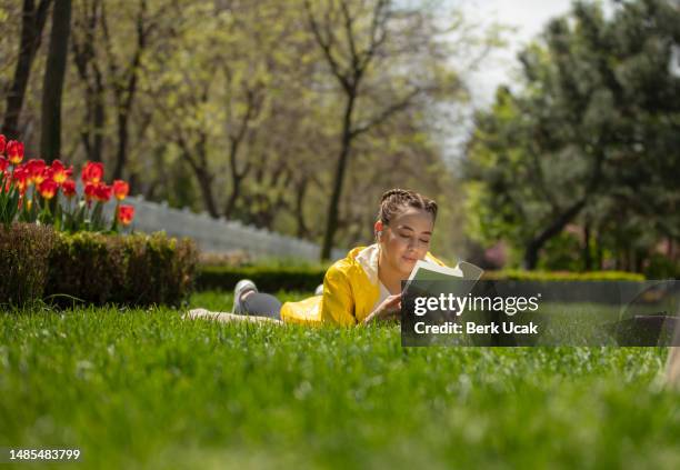 bella ragazza sta leggendo un libro sull'erba del parco pubblico in primavera. - libri gialli estate foto e immagini stock