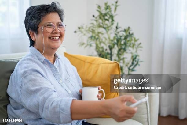 asian senior woman uses a remote to turn on the air conditioner. - ac weary stockfoto's en -beelden