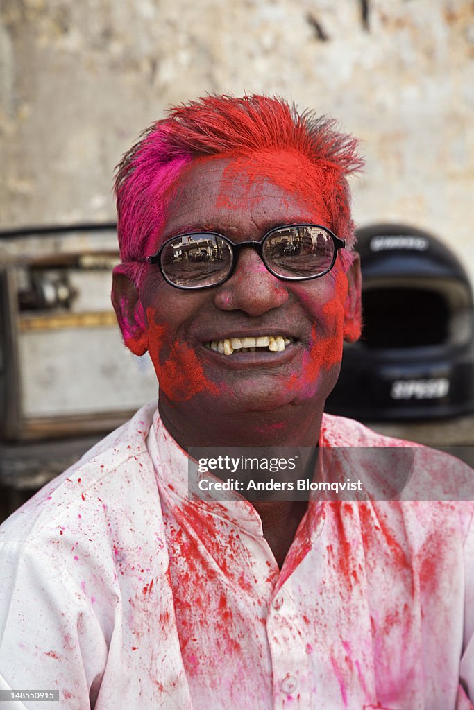 Portrait of elderly man with painted red face at the Holi festival.