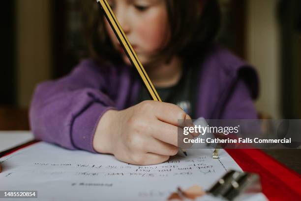 focus on a pencil that a little girl holds as she does homework - escribir a mano fotografías e imágenes de stock