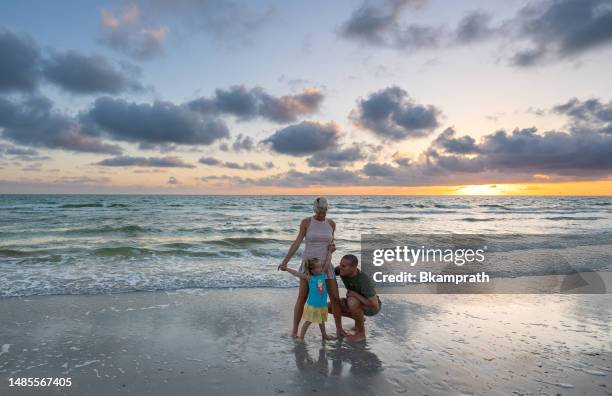 father, mother, and daughter playing during a vibrant sunset at treasure island beach on the gulf coast of florida usa - clearwater stock pictures, royalty-free photos & images