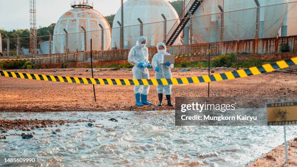 two scientists in a protective suit takes a sample of water from the river after the release of chemical waste. - microbiologist stock pictures, royalty-free photos & images