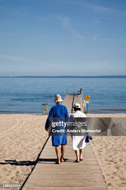 elderly couple heading down the beach for swim. - skane stock pictures, royalty-free photos & images