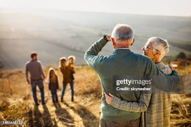 rückansicht des umarmten älterenpaares, das ihre familie in der natur betrachtet. - familie mit mehreren generationen stock-fotos und bilder