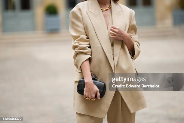 Beatrice Granno wears a gold large chain necklace, a beige linen V-neck / buttoned suit gilet, a matching beige linen blazer jacket, matching beige...