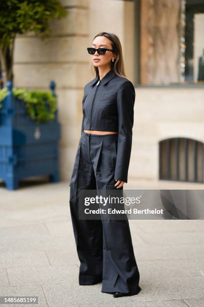 Guest wears black sunglasses from Celine, silver earrings, a black zipper / cropped jacket, matching black wide legs cargo pants, black shiny leather...