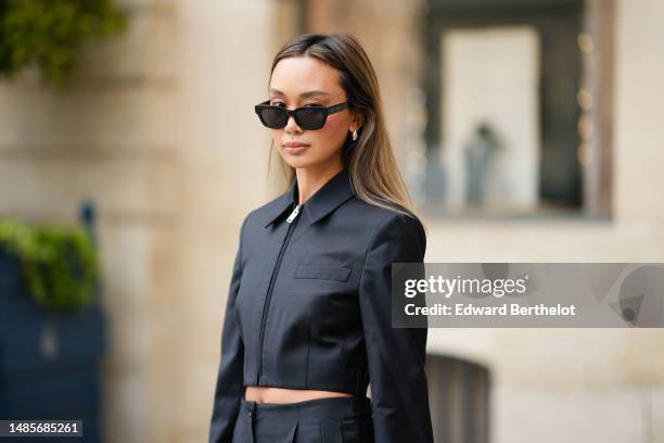 Guest wears black sunglasses from Celine, silver earrings, a black zipper / cropped jacket, matching black wide legs cargo pants, outside the COS...