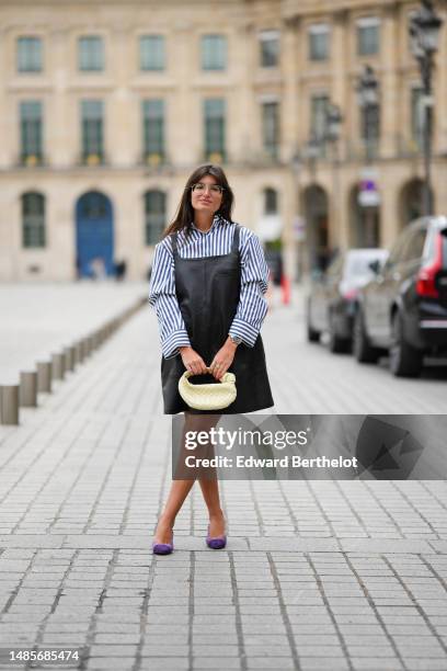 Guest wears silver metallic sunglasses, a navy blue and white striped print pattern cotton shirt, a black shiny leather tank-top / short dress, a...