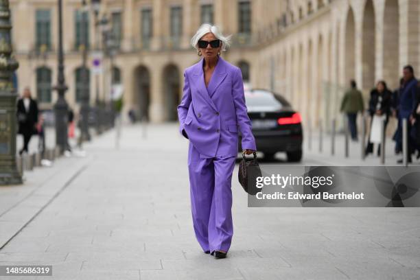 Grece Ghanem wears black sunglasses from Saint Laurent, a beige leather and gold braided earrings, a purple oversized blazer jacket, matching purple...