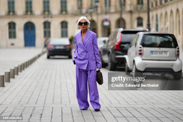 Grece Ghanem wears black sunglasses from Saint Laurent, a beige leather and gold braided earrings, a purple oversized blazer jacket, matching purple...