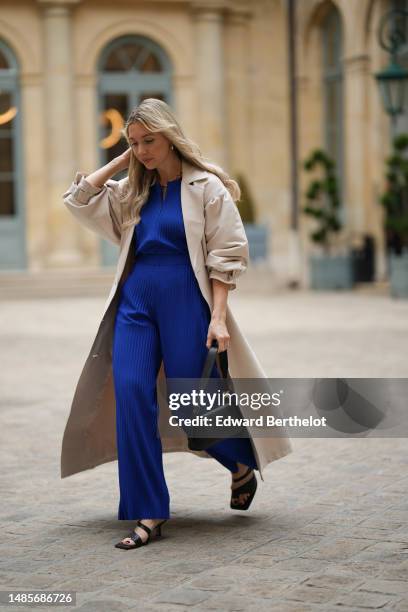 Guest wears gold earrings, a gold large chain necklace, a royal blue striped embossed pattern zipper neck / belted / flowing jumpsuit, a beige...