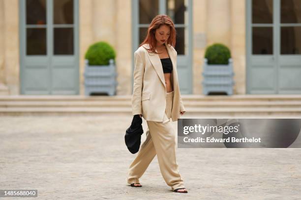 Guest wears small gold piercing, gold earrings, a silver small necklace, a beige linen long blazer jacket, matching beige linen large suit pants, a...