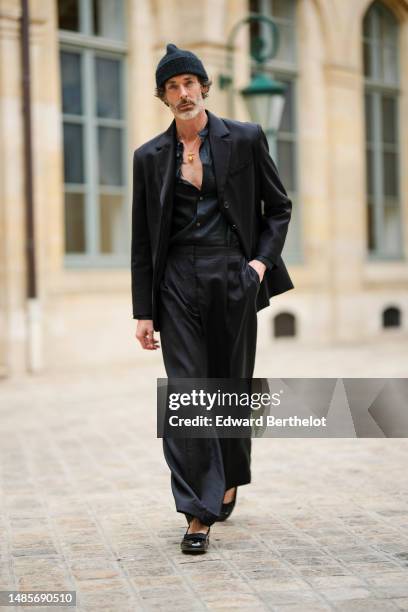 Richard Biedul wears a black wool ribbed beanie, a gold chain with a large pendant necklace, a black linen shirt, a black buttoned blazer jacket,...