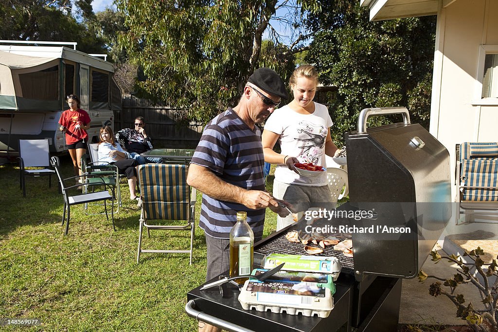 Family cooking barbeque in back garden.