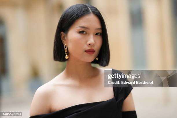 Meng Zhang wears gold large ball pendant earrings, a black asymmetric shoulder-off / long sleeves / cropped top, outside the COS show, on April 26,...