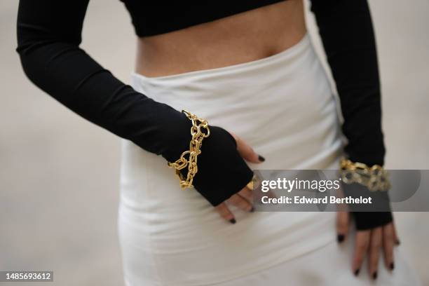 Meng Zhang wears a black asymmetric shoulder-off / long sleeves / cropped top, gold large bracelets, gold rings, a white high waist midi skirt,...