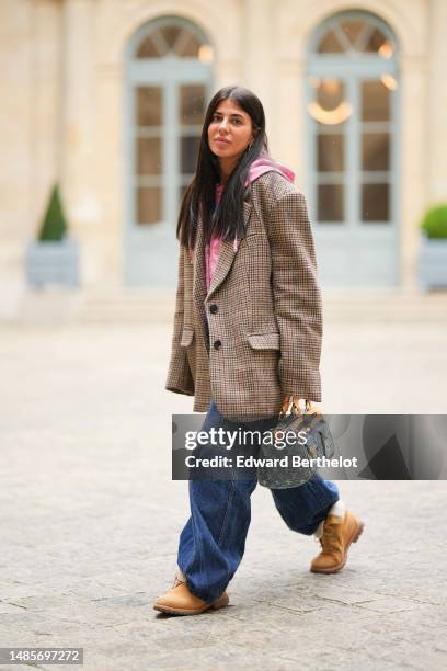 Heloise Salessy wears gold earrings, a pink with multicolored print pattern large t-shirt, a brown and black houndstooth print pattern wool oversized...