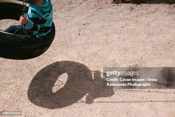 shadow of child swings on tire swing in sunshine in summer - tire swing stock pictures, royalty-free photos & images