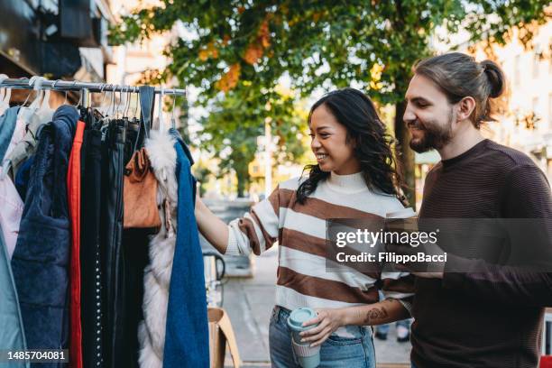 a millennial couple is taking a look at a second-hand clothing store - rommelmarkt stockfoto's en -beelden