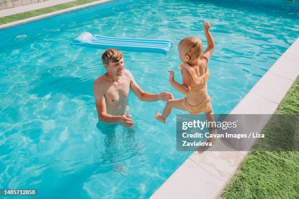 a two-year-old girl jumps from the side into the outdoor pool - 2 year old blonde girl father stock-fotos und bilder