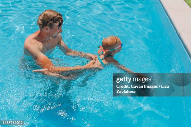 dad teaches two-year-old daughter to swim in the outdoor pool - 2 year old blonde girl father ストックフォトと画像
