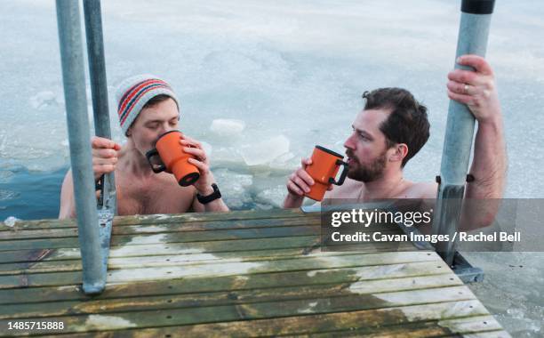 two friends drinking hot drink whilst cold water swimming - freeze motion stock-fotos und bilder