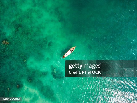 Aerial view with many long-tailed boats floating in the clear emerald green water known as Phuket Andaman Eggs until you can see the rocks under the sea below at Phuket, Thailand. Aerial view with many long-tailed boats floating in the clear emerald green water known as Phuket Andaman Eggs until you can see the rocks under the sea below at Phuket, Thailand.