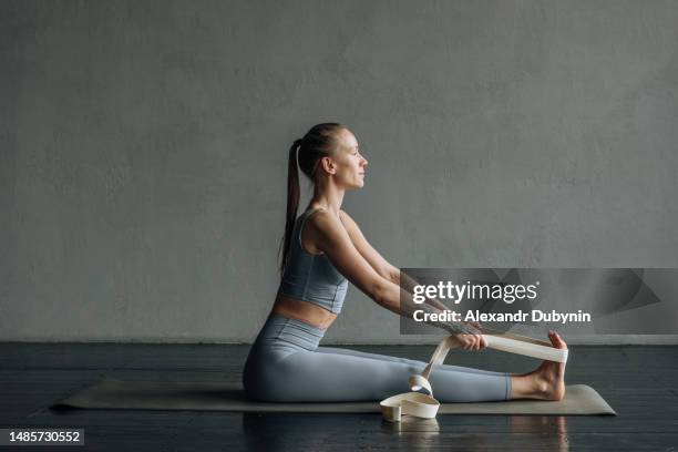 beautiful woman practicing yoga doing body stretching exercise with belt in yoga class - strap stock pictures, royalty-free photos & images