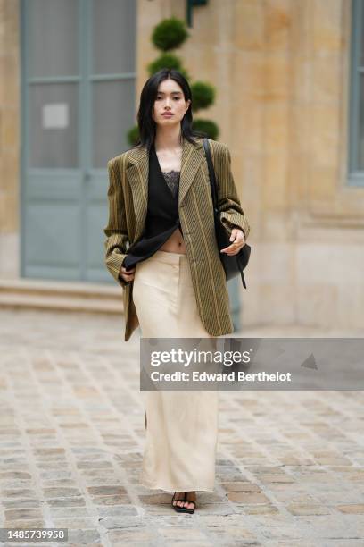 Guest wears a black lace flower print pattern shoulder-off top, a black linen buttoned gilet, a beige / green / pale yellow striped print pattern...