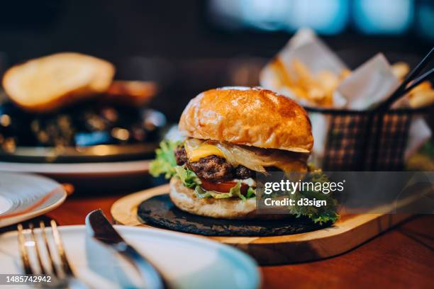 fresh delicious burger with french fries and salad served on rustic wooden board on table. a feast on the dining table in restaurant. food and lifestyle concept - burger stock-fotos und bilder