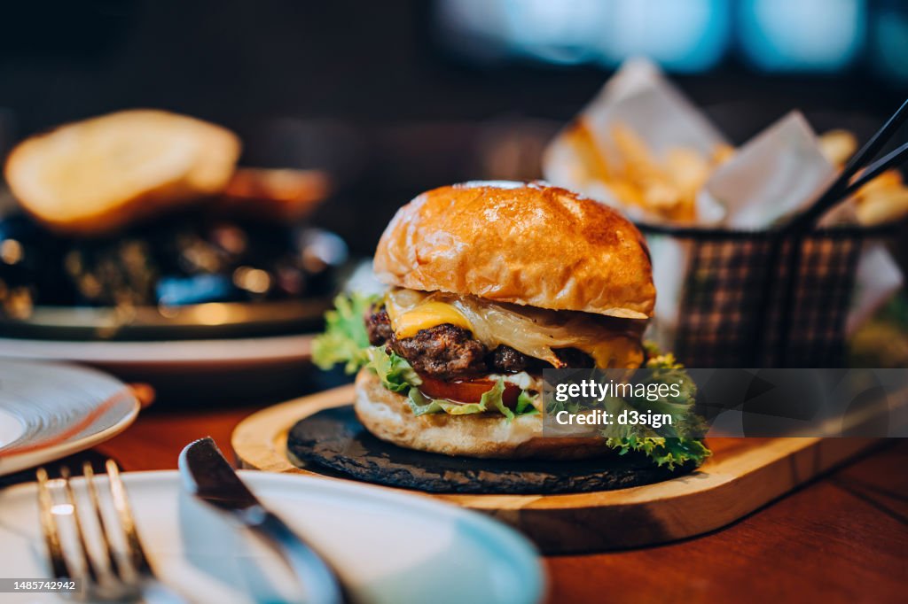Fresh delicious burger with french fries and salad served on rustic wooden board on table. A feast on the dining table in restaurant. Food and lifestyle concept