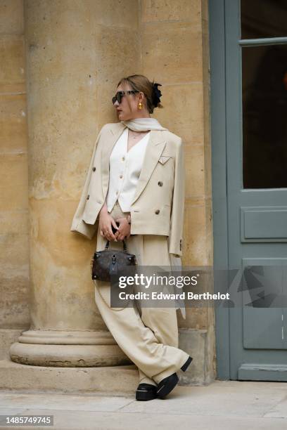 Guest wears black sunglasses from Chanel, gold earrings, a white silk scarf, a gold chain pendant necklace, a white tweed buttoned V-neck gilet...