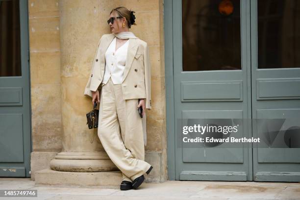 Guest wears black sunglasses from Chanel, gold earrings, a white silk scarf, a gold chain pendant necklace, a white tweed buttoned V-neck gilet...