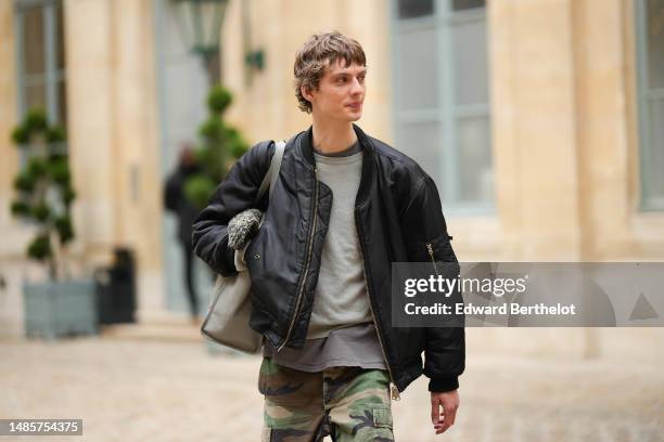 Guest wears a gray t-shirt, a pale gray wool pullover, a black nylon zipper oversized bomber coat, a pale gray shiny leather large shoulder bag,...