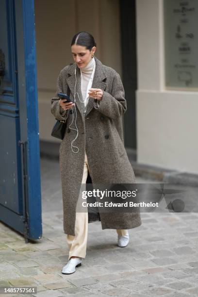 Guest wears gold earrings, a white latte turtleneck pullover, a white blazer jacket, a brown wool long oversized coat, pale yellow linen suit pants,...
