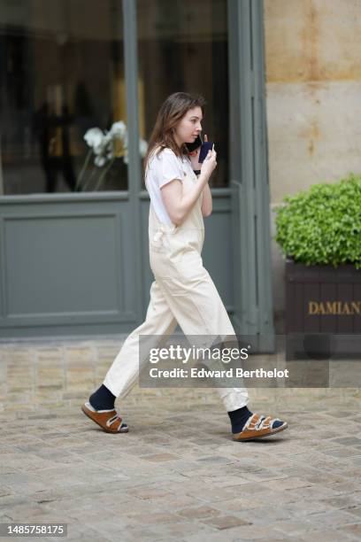 Guest wears silver earrings, silver rings, a white t-shirt, a white latte denim pair of overalls, black socks, brown camel suede and white sheep...