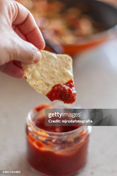 closeup of human hand holding a nacho with spicy sauce - tortilla chip stock-fotos und bilder