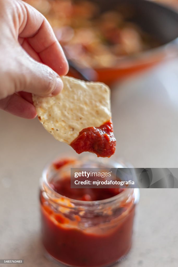 Closeup of human hand holding a nacho with spicy sauce