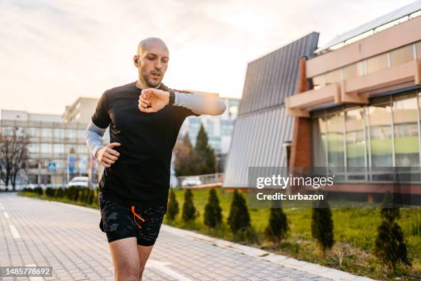 athlete checking fitness activity on fitness tracker while running outdoors - smartwatch imagens e fotografias de stock