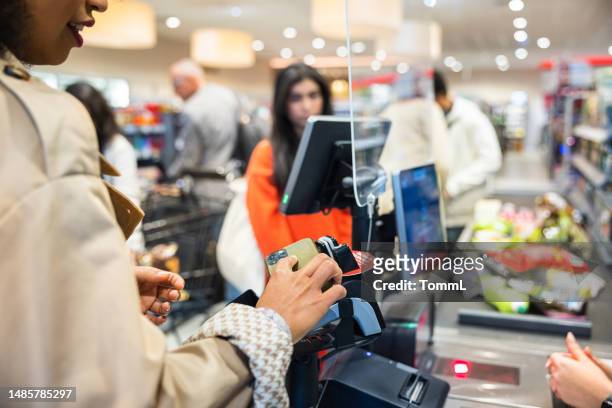 woman using contactless to pay for groceries at checkout - checkout conveyor belt stock pictures, royalty-free photos & images