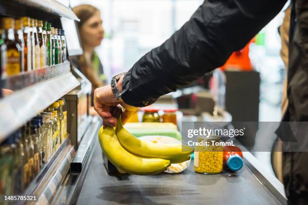 person putting bananas on conveyor at store  checkout - products stock pictures, royalty-free photos & images