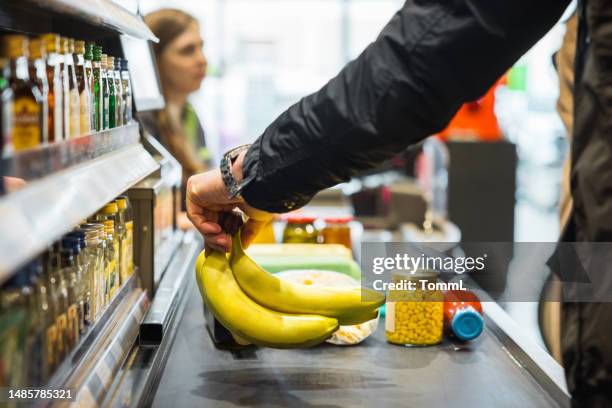person putting bananas on conveyor at store checkout - balcão de pagamento imagens e fotografias de stock